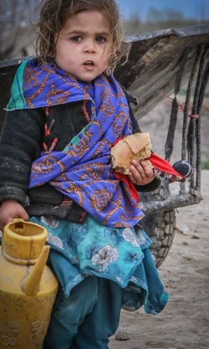 Portrait of a child in Afghanistan holding a piece of bread and a yellow jug, showcasing rural life.